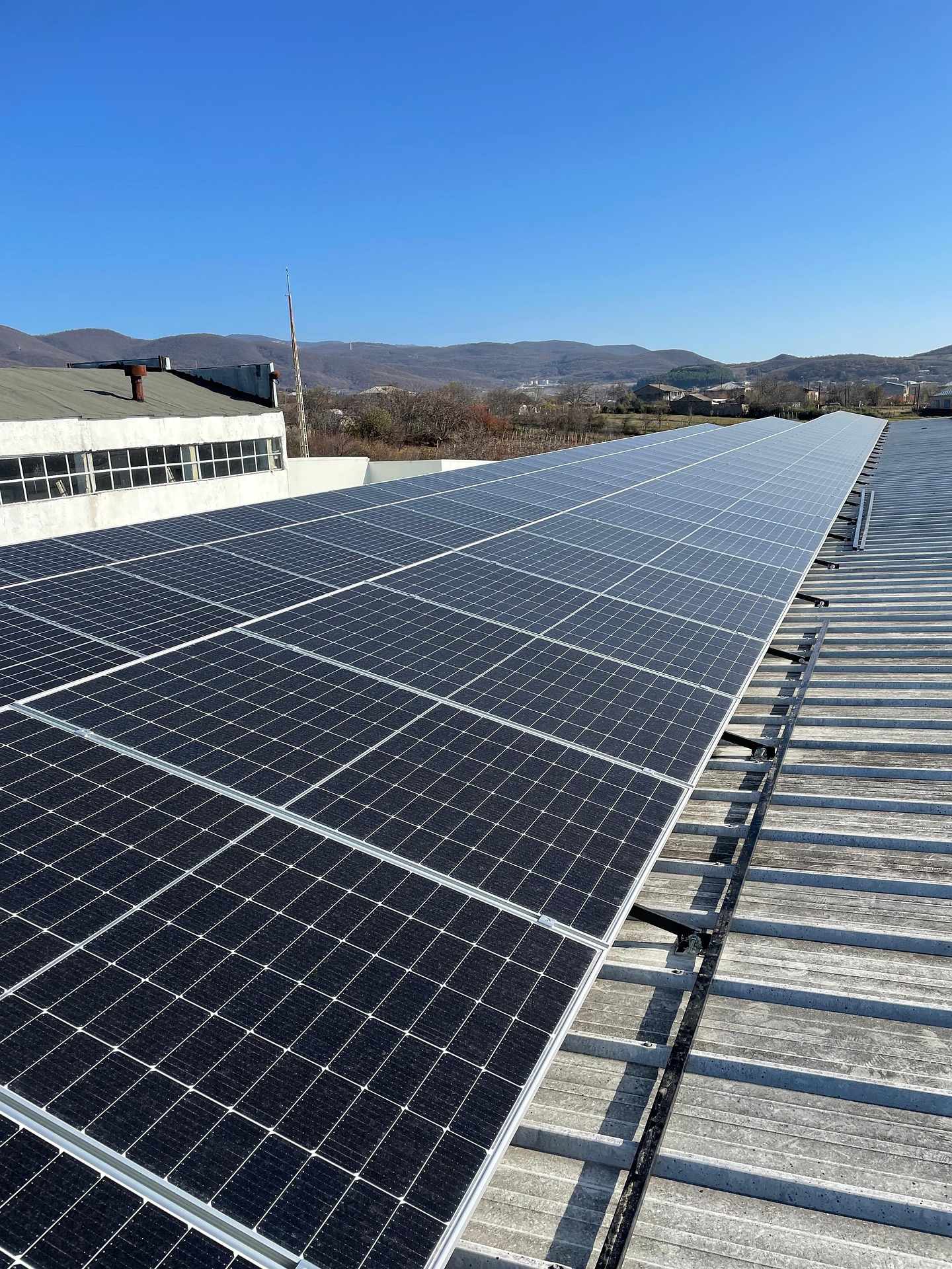 Photovoltaikanlage auf dem Trapezblechdach einer Gewerbehalle, im Hintergrund eine Hügellandschaft
